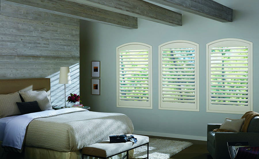 Arched windows in bedroom with interior shutters.