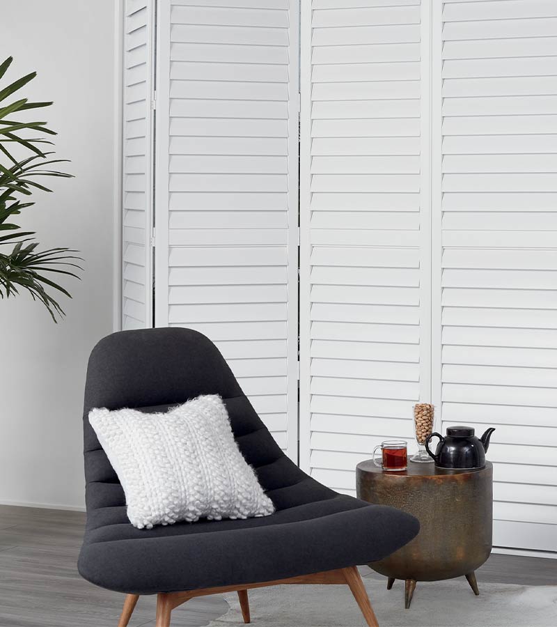 bi-fold custom white shutters behind lounge chair