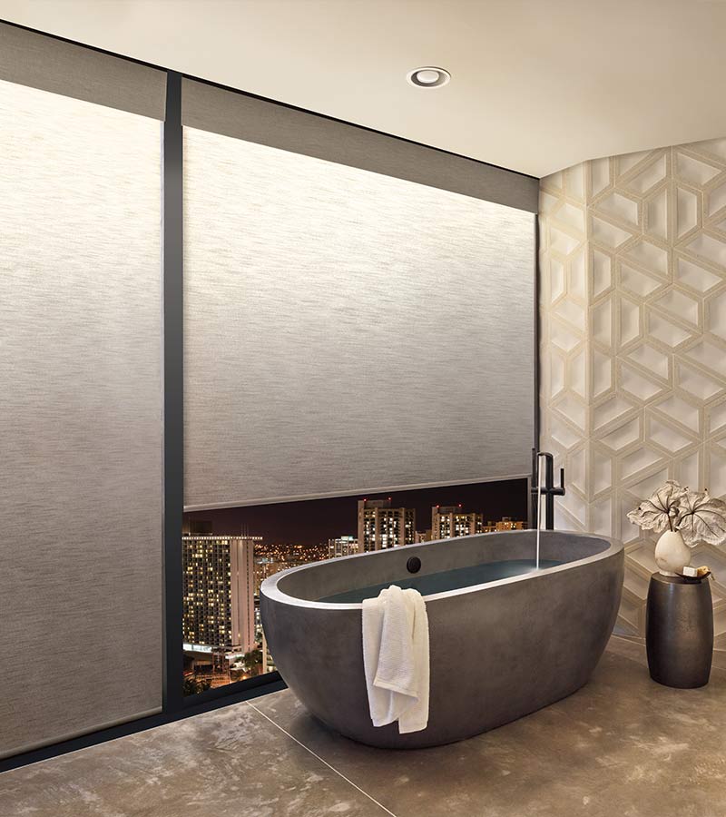 a modern bathroom with a tub next to large windows covered by illuminated privacy shades