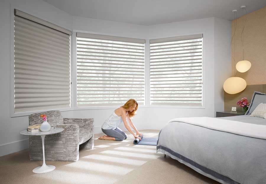 person rolling up yoga mat by window with white window shades