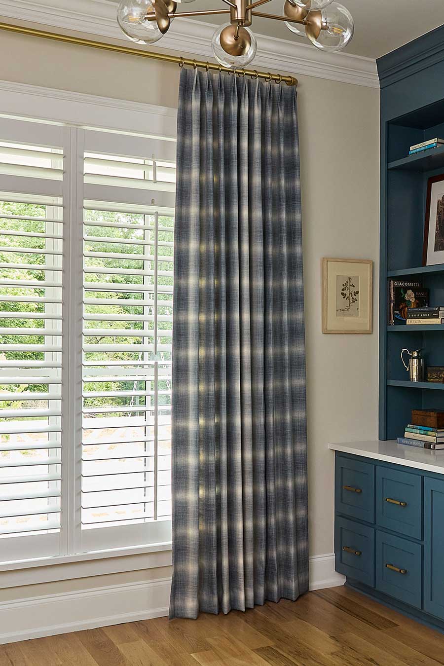 Custom drapery hanging on a gold rod above long windows overlooking a green backyard